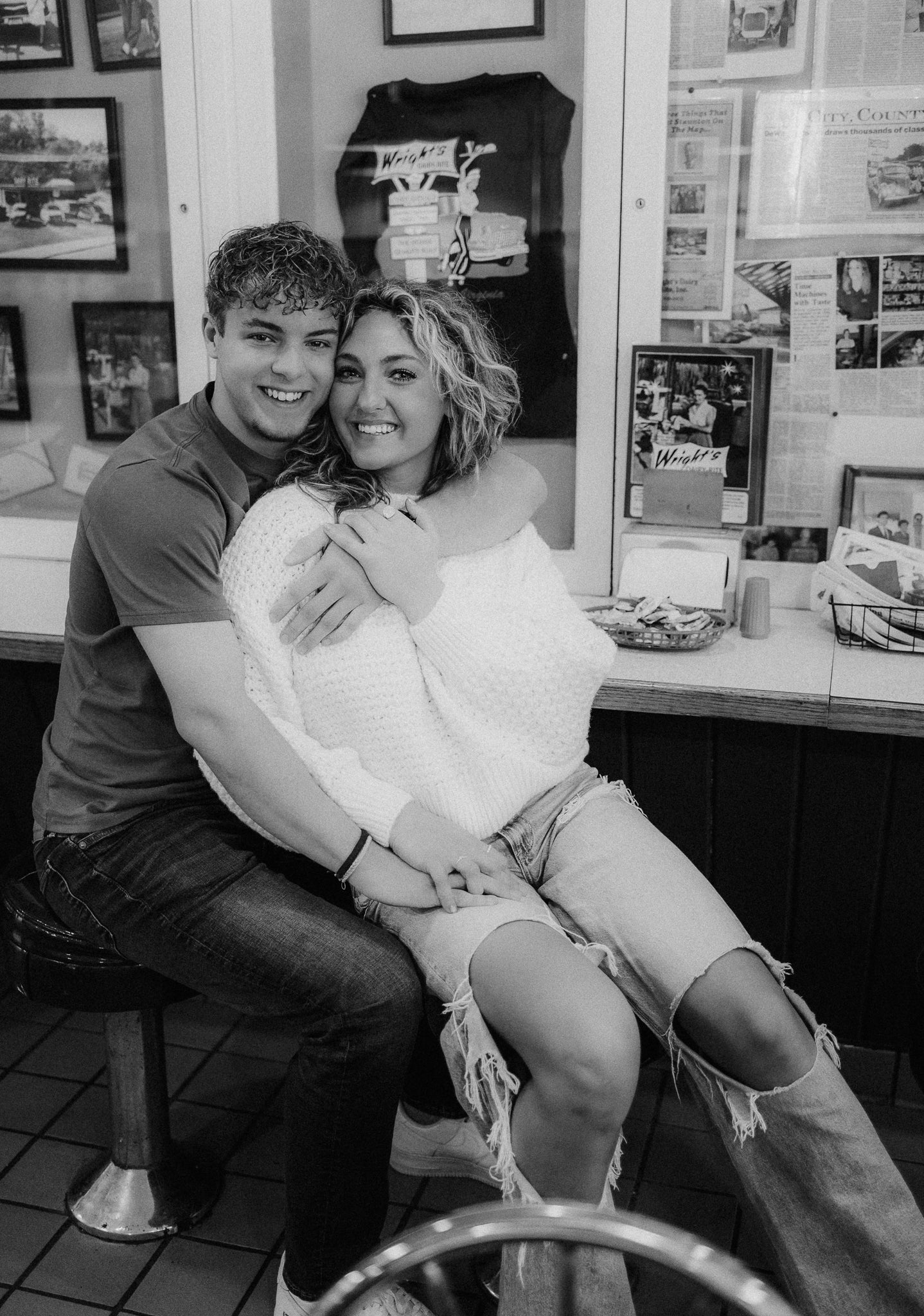 Black and white photo of a smiling couple sitting together in a cozy diner-style setting.
